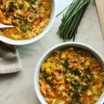 Lentil stew in bowls with tomatoes on the side and chive garnish