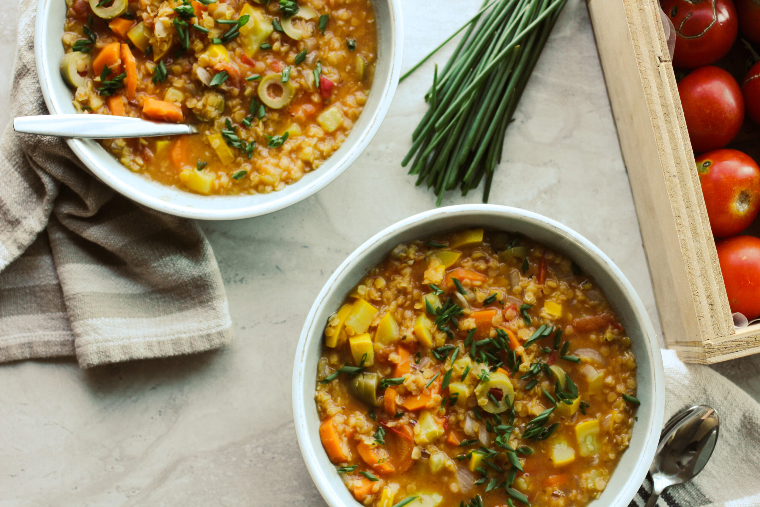 Lentil stew in bowls with tomatoes on the side and chive garnish