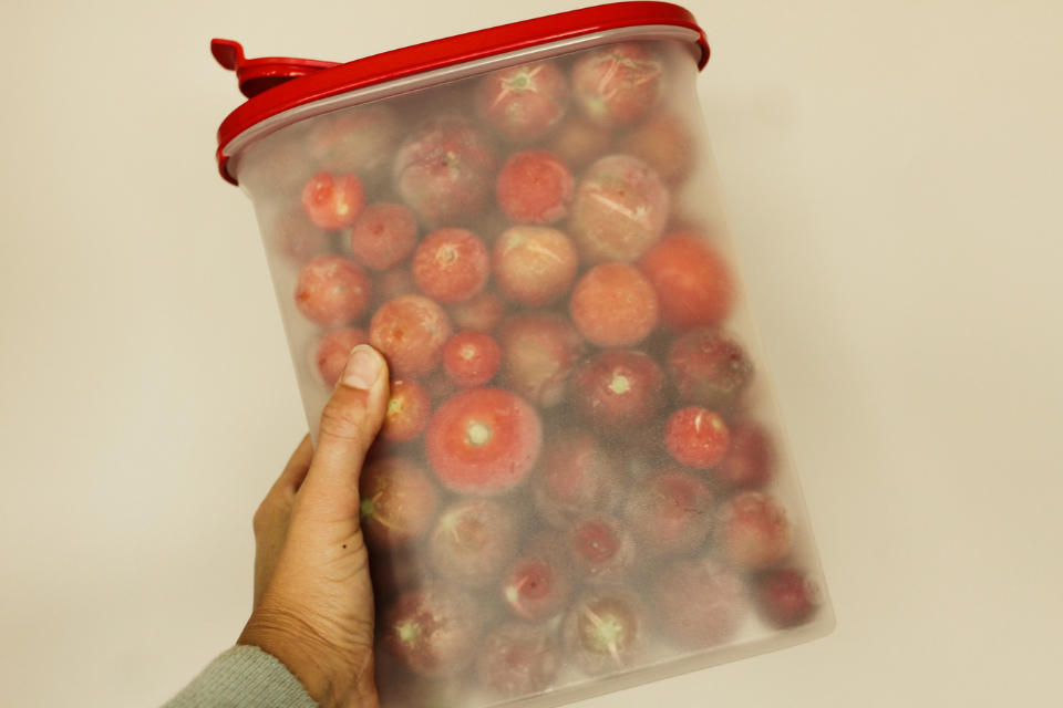 Whole frozen tomatoes in a plastic container