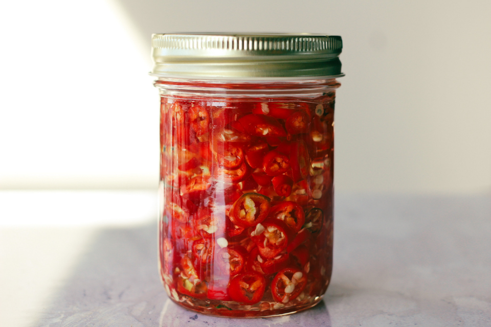 Jar filled with oil and red chilli peppers on a white granite countertop